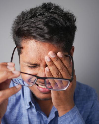 A man takes his glasses off and has one hand over a painful eye post-tooth extraction